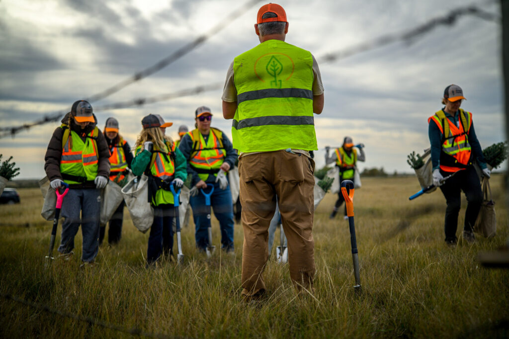 A planting crew in high-visibility vests walks a field with planting shovels