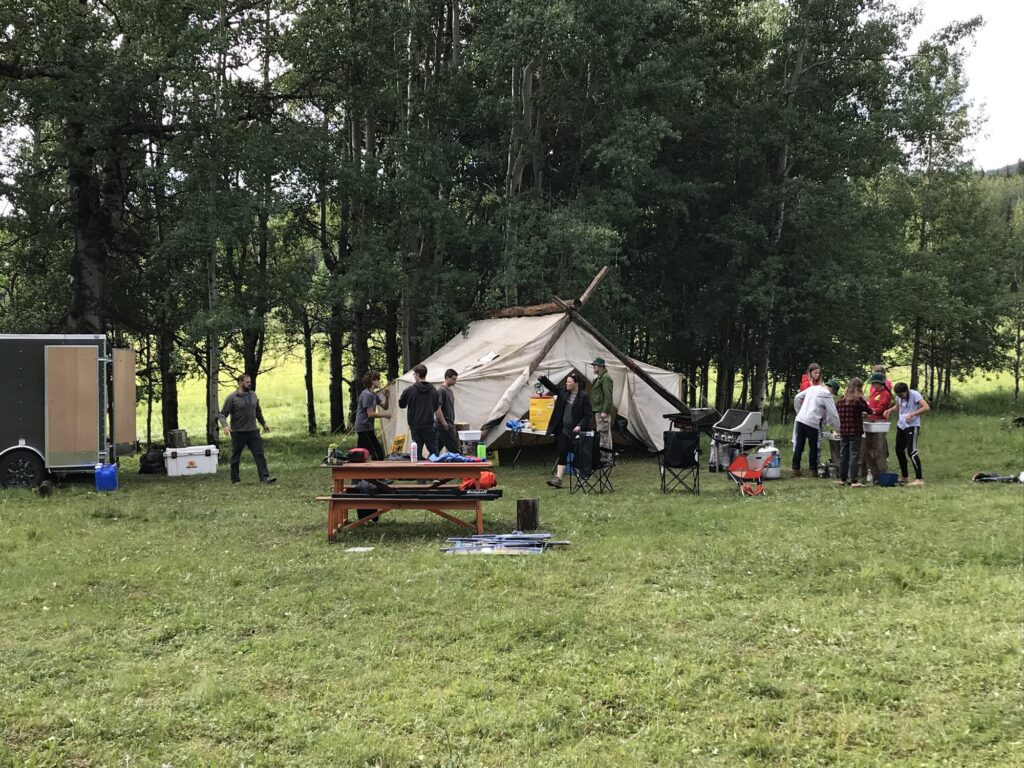 Families gathered around a canvas tent at a forest camp