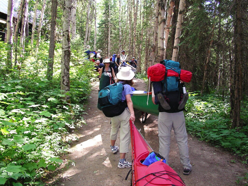 Hikers with packs carrying a kayak along a forest trail